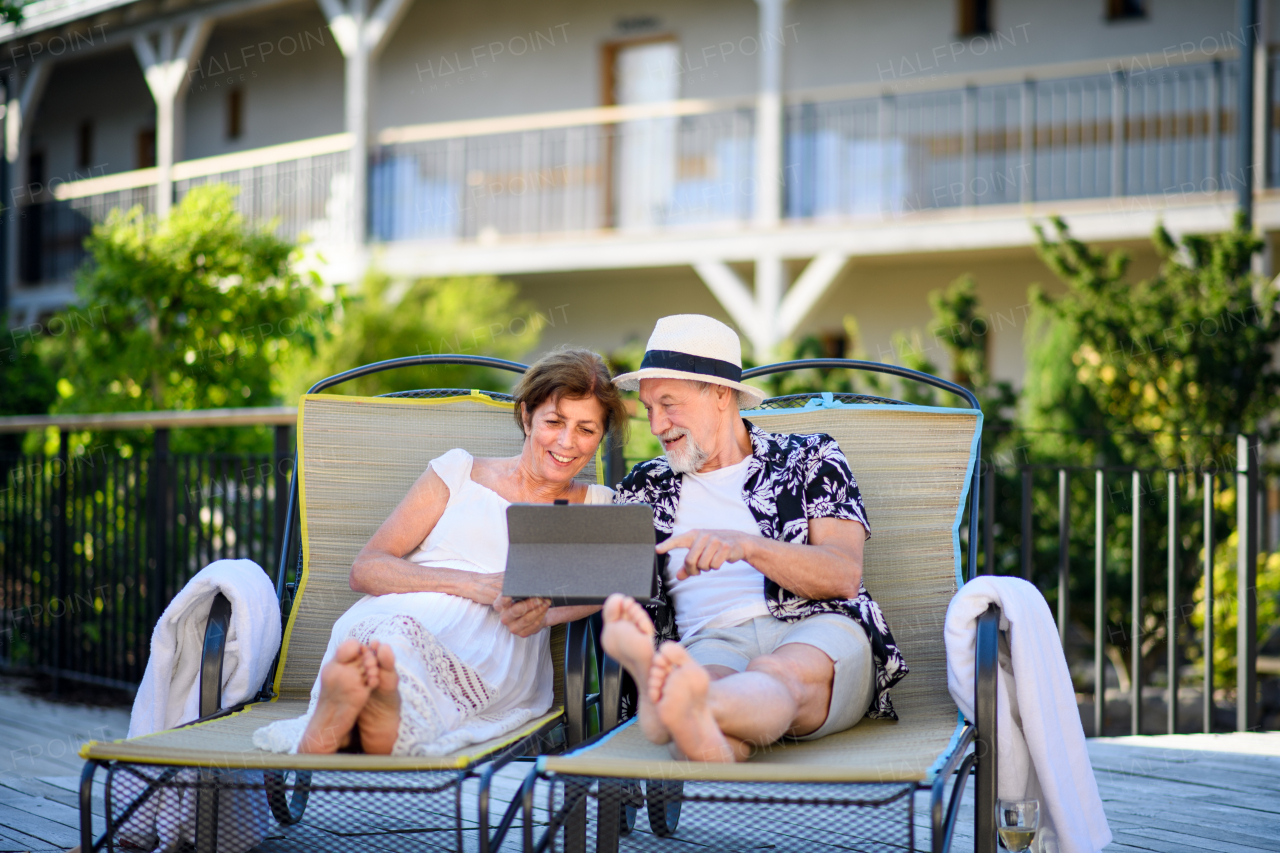 Portrait of senior couple with tablet outdoors on holiday, relaxing.