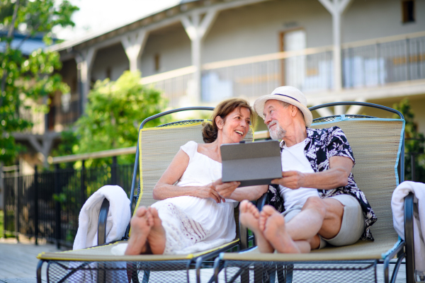 Portrait of senior couple with tablet outdoors on holiday, relaxing.