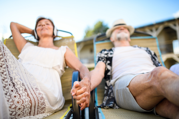 Front view of senior couple with headphones outdoors on holiday, relaxing.