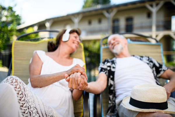 Front view of senior couple with headphones outdoors on holiday, relaxing.