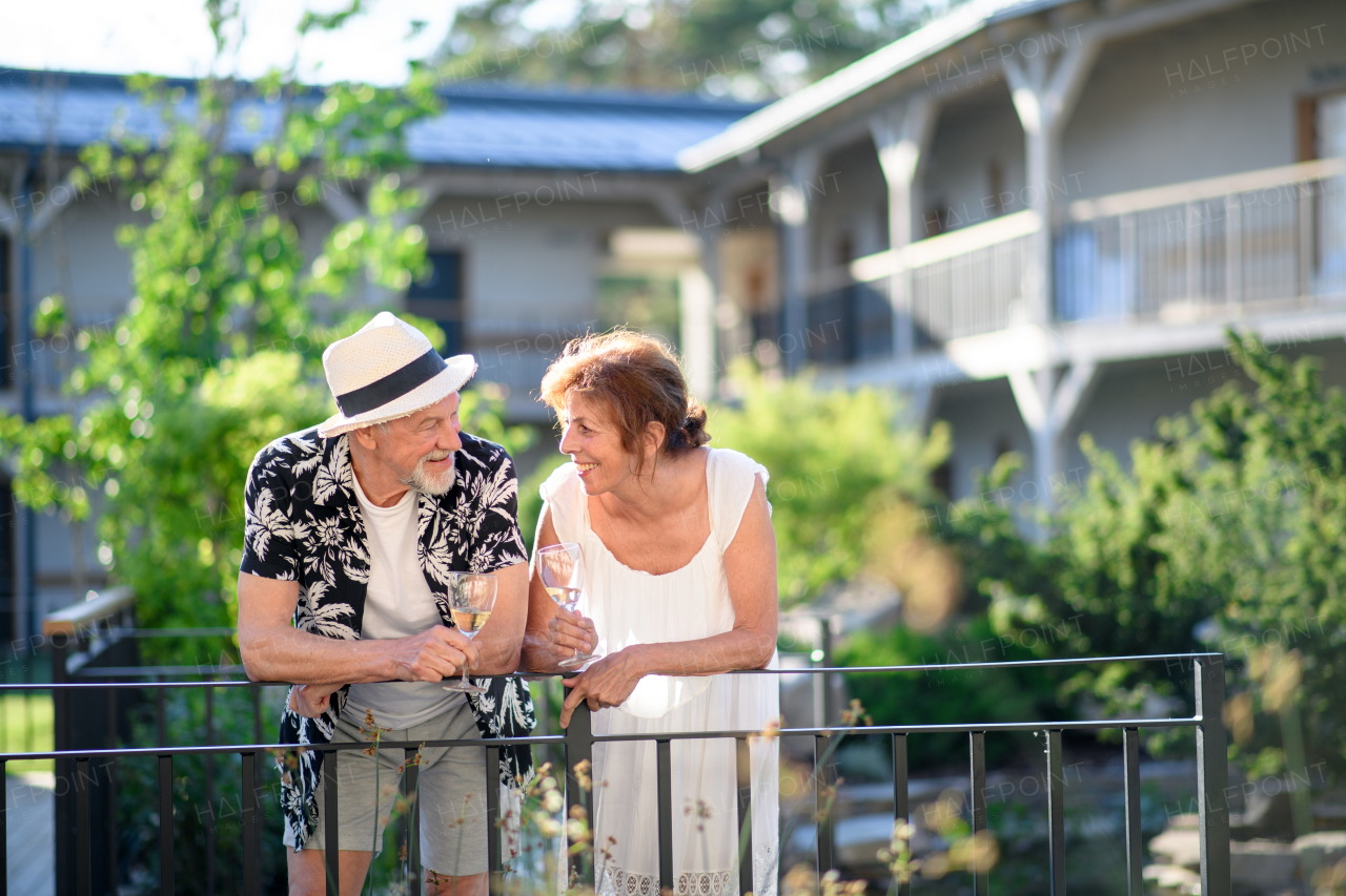 A senior couple holding wine outdoors on holiday, talking.