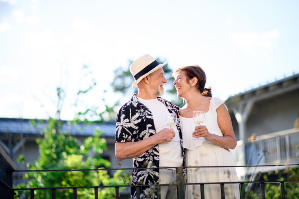 Portrait of senior couple in love holding wine outdoors on holiday, talking.