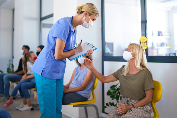 Portrait of nurse with face masks talking to patients in waiting room, coronavirus, covid-19 and vaccination concept.