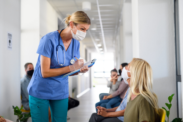 Portrait of nurse with face masks talking to patients in waiting room, coronavirus, covid-19 and vaccination concept.