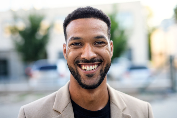 Front view portrait of african-american man standing outdoors in city, looking at camera.