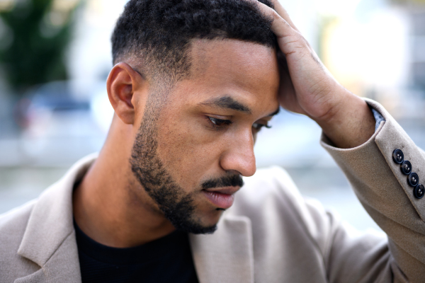 Front view portrait of african-american man standing outdoors in city, looking at camera.