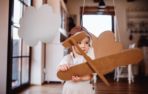 A toddler girl with carton plane and clouds playing indoors at home, flying concept.