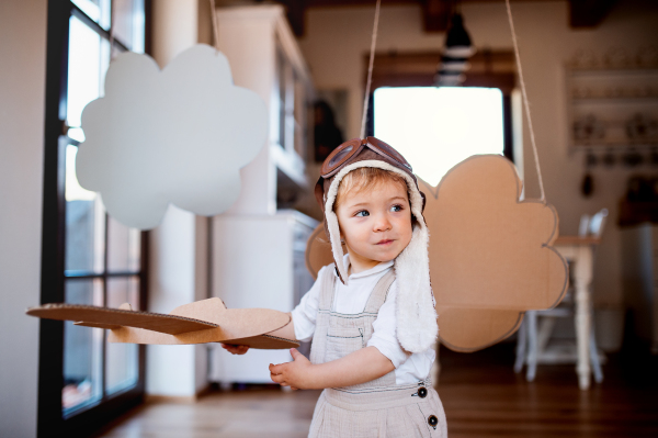 A toddler girl with carton plane and clouds playing indoors at home, flying concept.