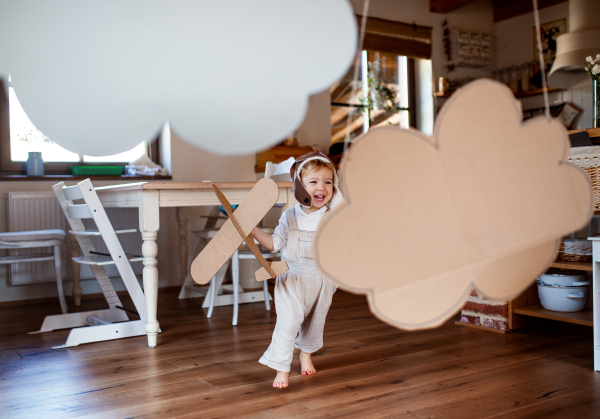 A toddler girl with carton plane and clouds playing indoors at home, flying concept.