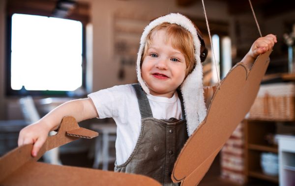 A happy toddler boy with carton plane playing indoors at home, flying concept.