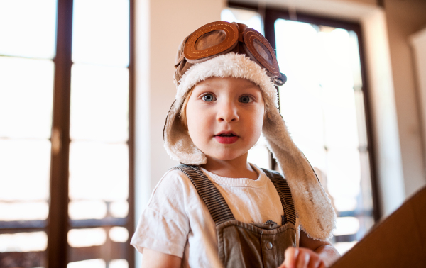 A happy toddler boy with carton plane playing indoors at home, flying concept.