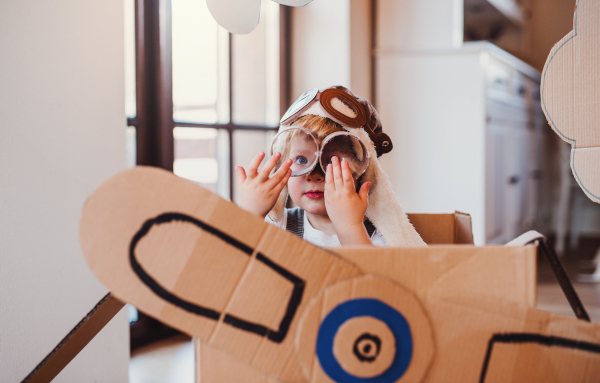 A happy toddler boy with carton plane playing indoors at home, flying concept.