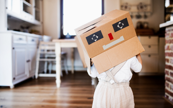 A toddler girl with carboard monster on head playing indoors at home.