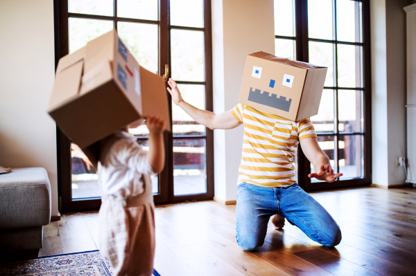 A happy toddler girl with a father and cardboard monster playing indoors at home.