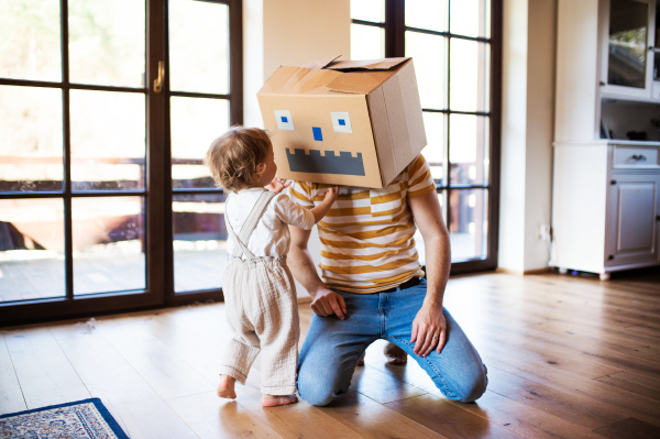 A happy toddler girl with a father and carboard monster playing indoors at home.