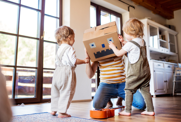 Two happy toddler children with a father and carboard monster playing indoors at home.