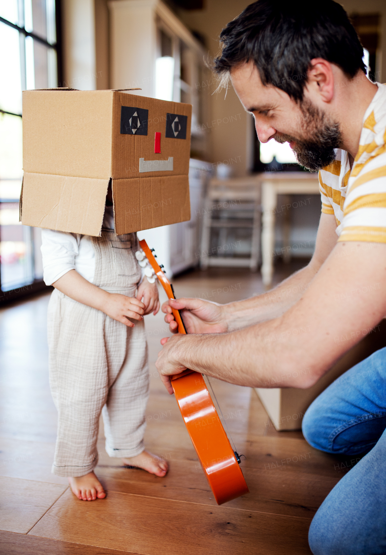 A happy toddler girl with a father and cardboard monster playing indoors at home.