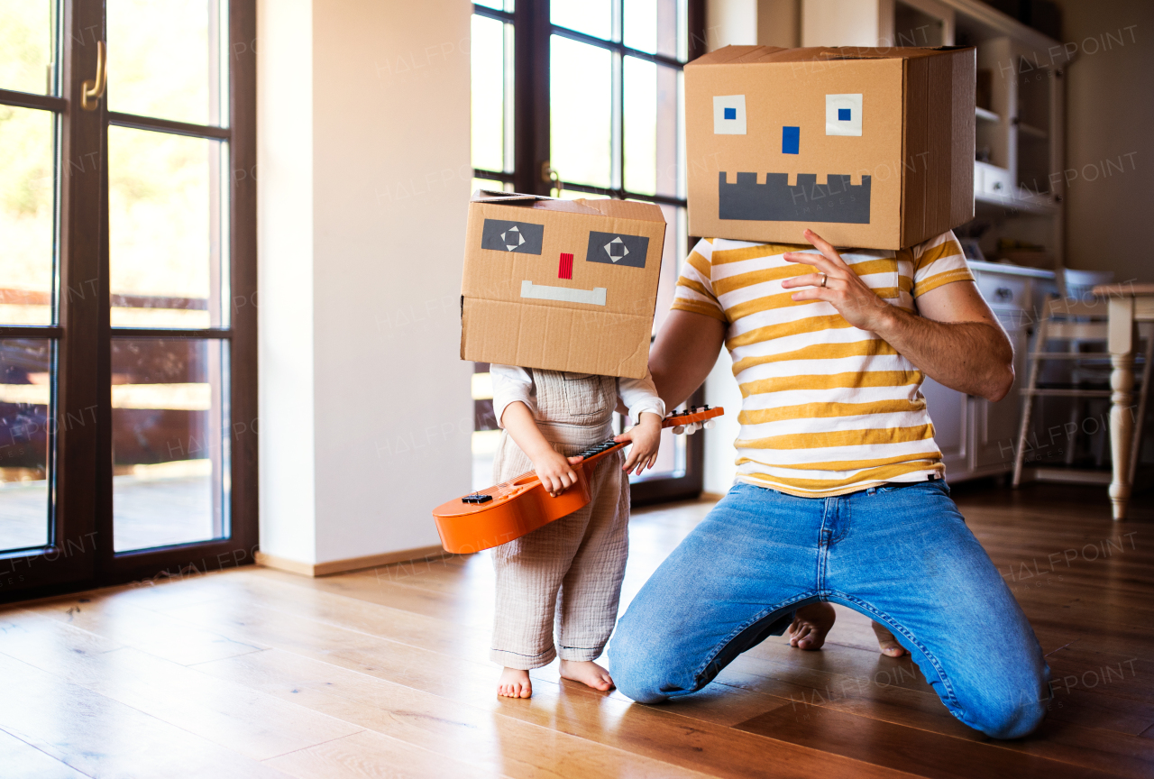 A happy toddler girl with a father and carboard monster playing indoors at home.