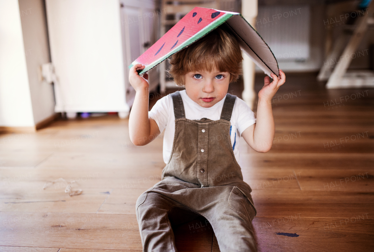 A toddler boy playing with large toy fruit indoors at home, looking at camera.