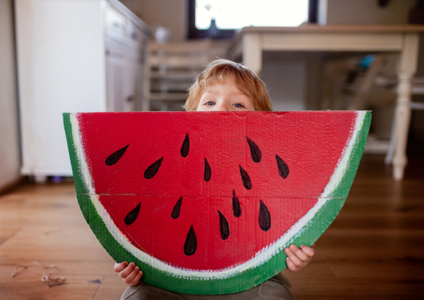 A toddler boy playing with large toy fruit indoors at home, eating fruit concept.