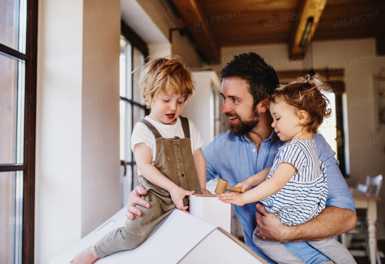 Two happy toddler children with father playing with paper house indoors at home.