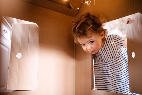 A toddler girl playing with paper house indoors at home. Copy space.