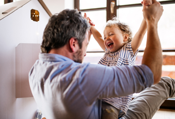 Two happy toddler children with a father and carboard house playing indoors at home.