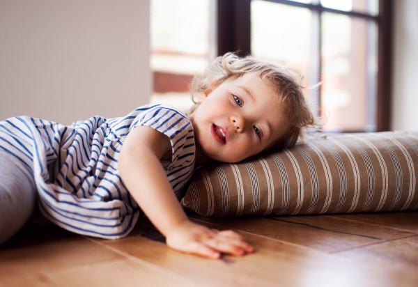 A happy toddler girl lying on the floor indoors at home, playing.