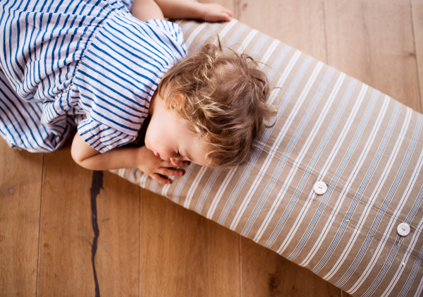 A top view of a toddler girl lying on the floor indoors at home, sleeping.