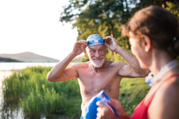 Senior couple in swimsuit standing by lake outdoors before swimming. Copy space.