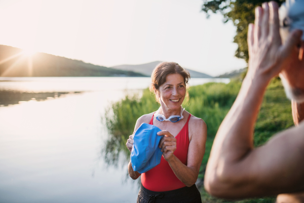 Senior couple in swimsuit standing by lake outdoors before swimming. Copy space.