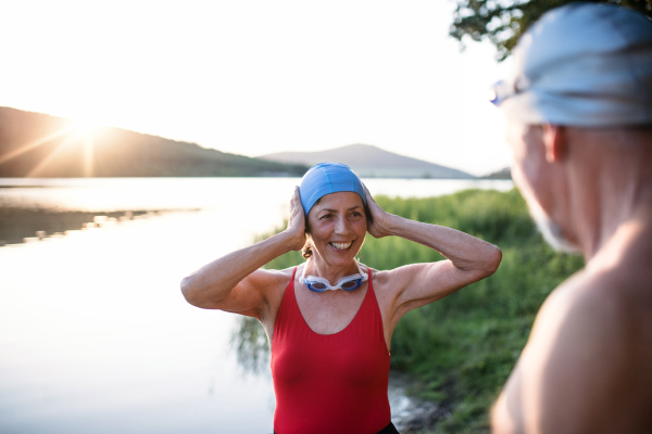 Senior couple in swimsuit standing by lake outdoors at sunset before swimming. Copy space.