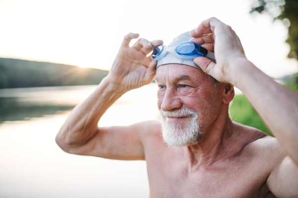 Cheerful senior man in swimsuit standing by lake outdoors before swimming.