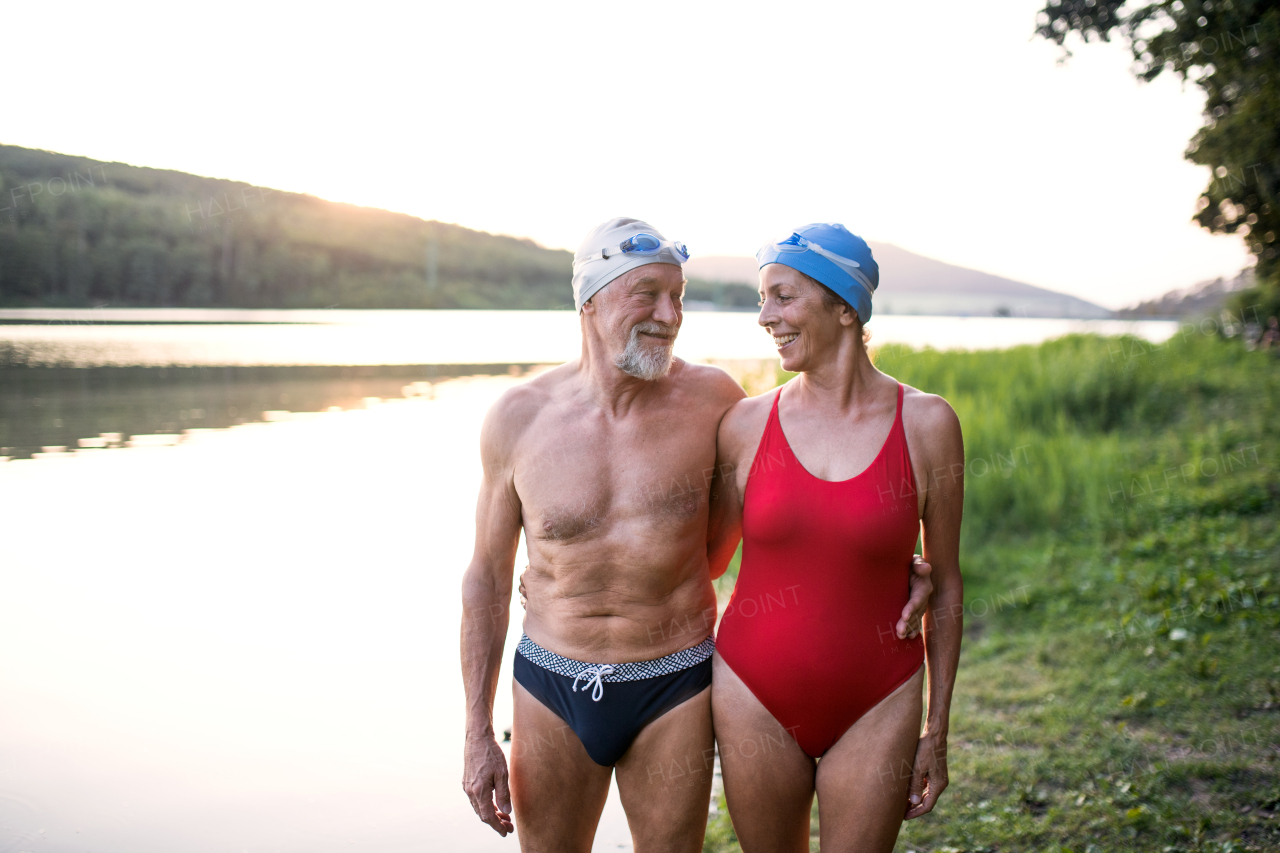 Senior couple in swimsuit standing by lake outdoors before swimming. Copy space.