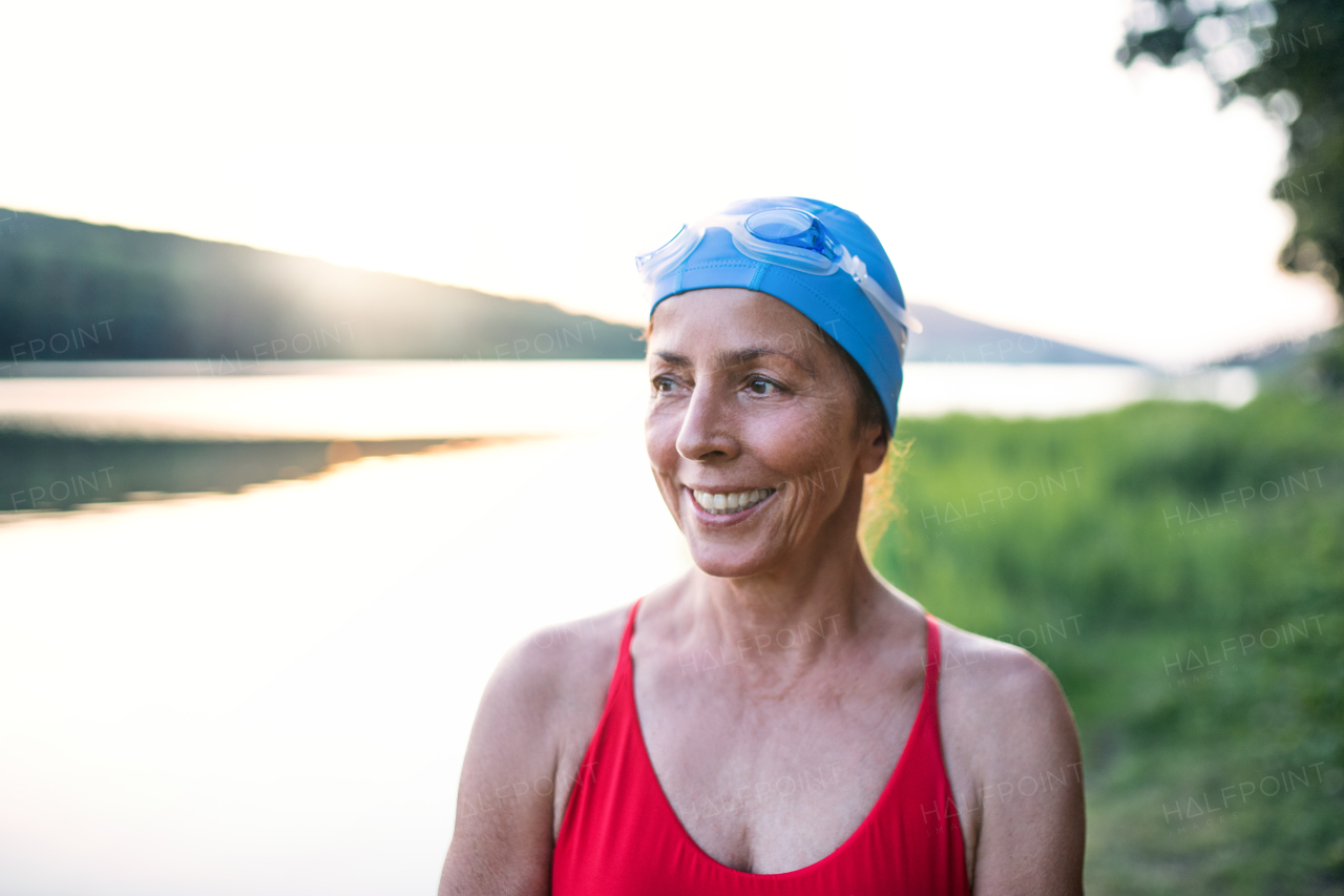 Cheerful senior woman in swimsuit standing by lake outdoors before swimming.