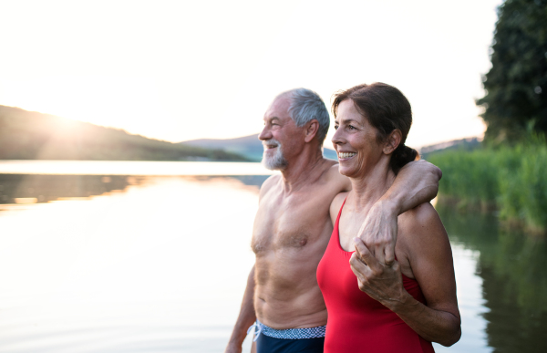 Senior couple in swimsuit standing by lake outdoors before swimming. Copy space.