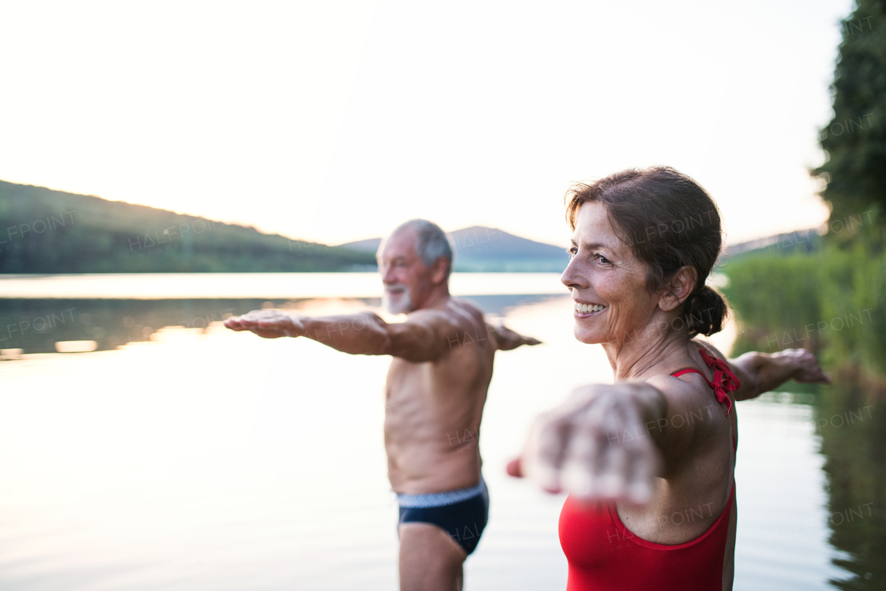 Senior couple in swimsuit standing in lake outdoors before swimming, doing exercise.