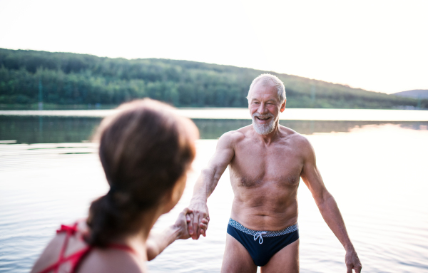 Cheerful senior couple in swimsuit standing in lake outdoors before swimming.