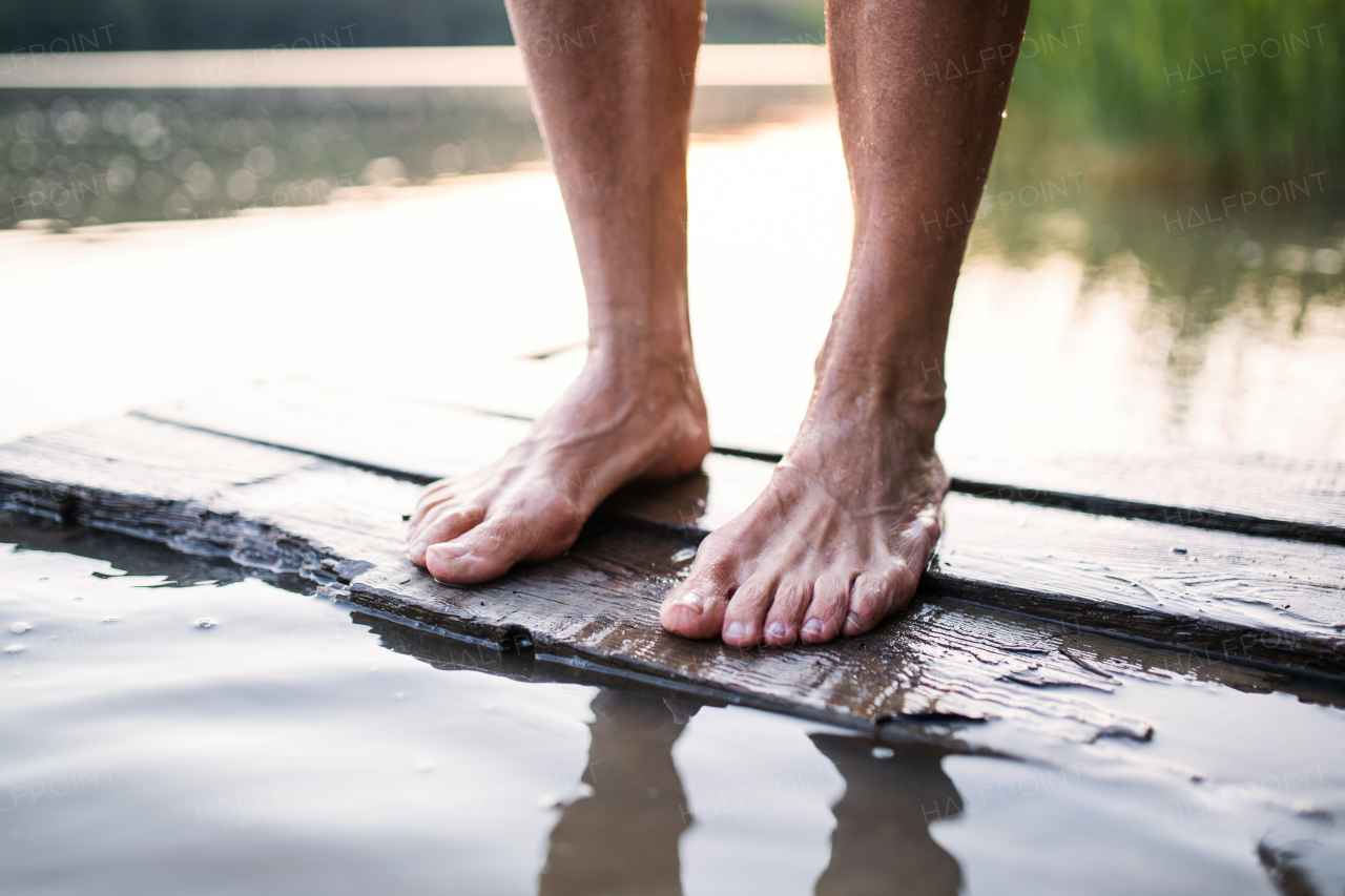 Bare feet of woman standing by lake outdoors before swimming, midsection.