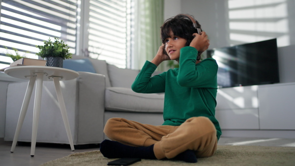 A happy multiracial boy with headphones and smartphone listening to music at home.