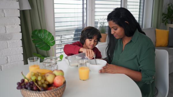 A happy little boy having breakfast with his mother at home.