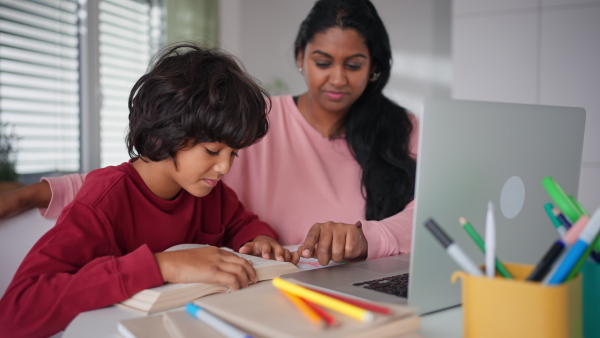 A little multiracial boy doing homework with his mother at home.