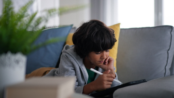 A little multiracial boy with tablet lying on sofa at home.