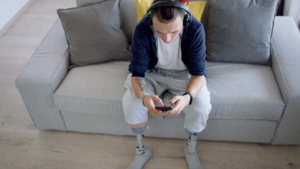 Top view of disabled young man using smartphone indoors at home, leg prosthetic concept.