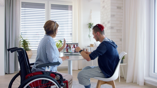 A rear view of disabled people sitting at the table indoors at home, video call concept.