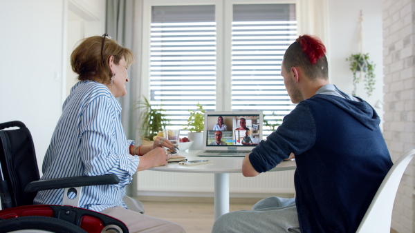 A rear view of disabled people sitting at the table indoors at home, video call concept.