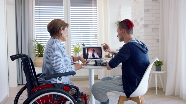 A rear view of disabled people sitting at the table indoors at home, video call concept.