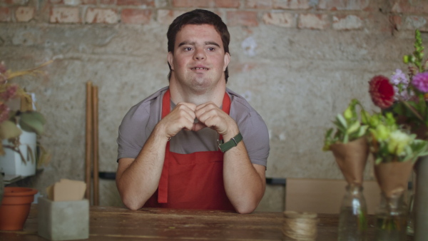 A young male florist with Down syndrome standing indoors in flower shop and looking at camera