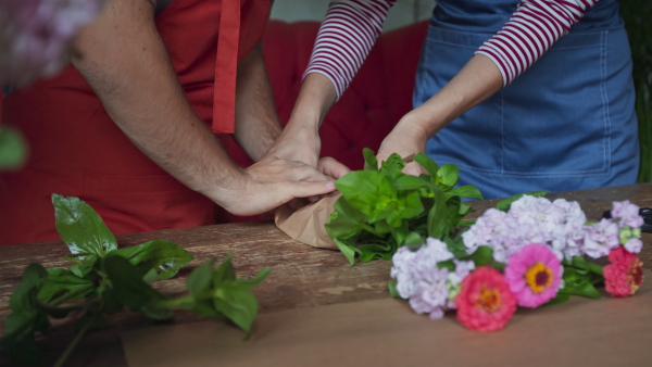 A close up of young male florist with Down syndrome working with help of mentoring colleague indoors in flower shop