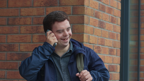 A close up of happy man with Down syndrome making phone call outdoors.